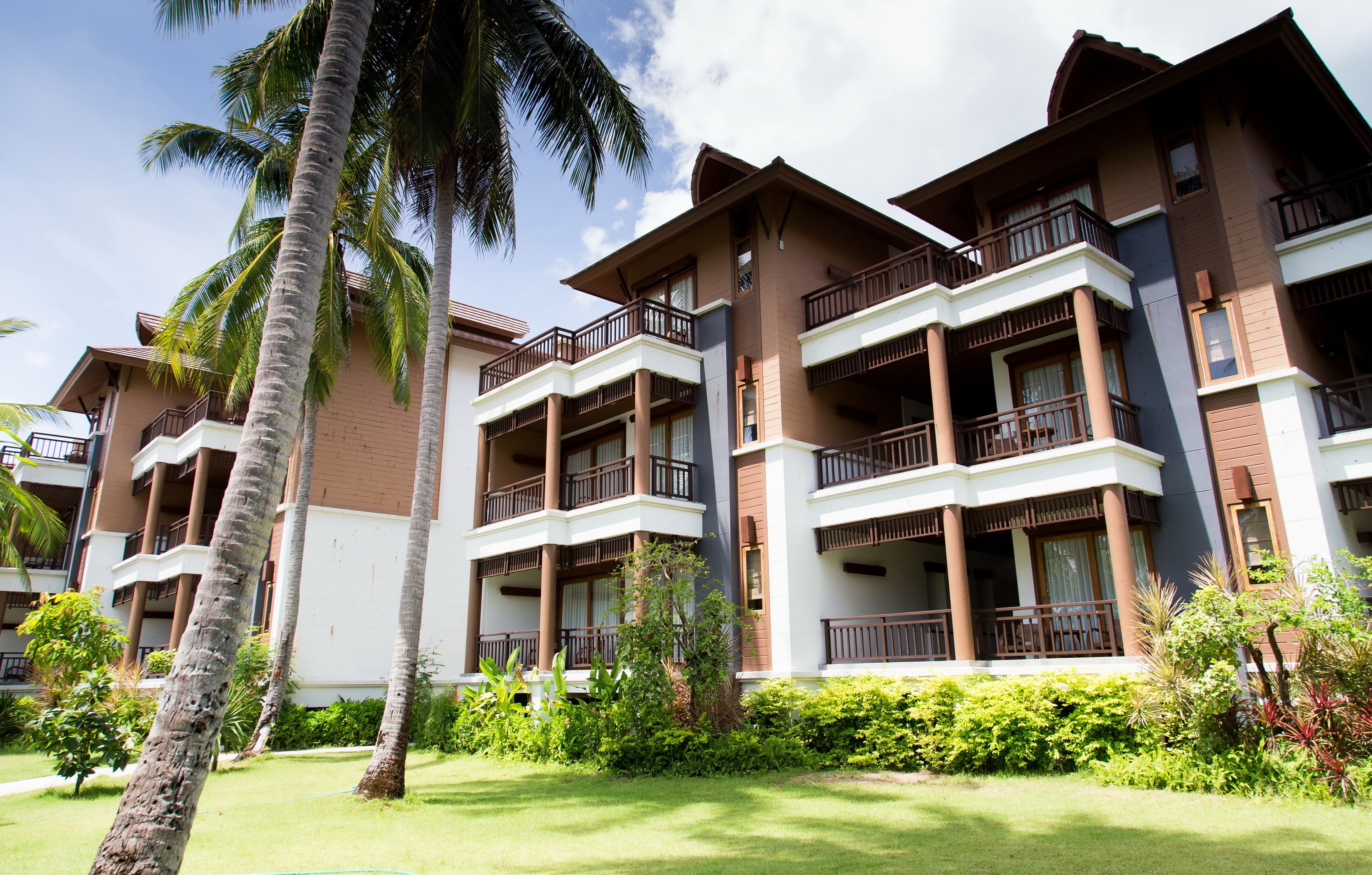 A multi-story hotel with balconies, palm trees, and a well-maintained lawn.