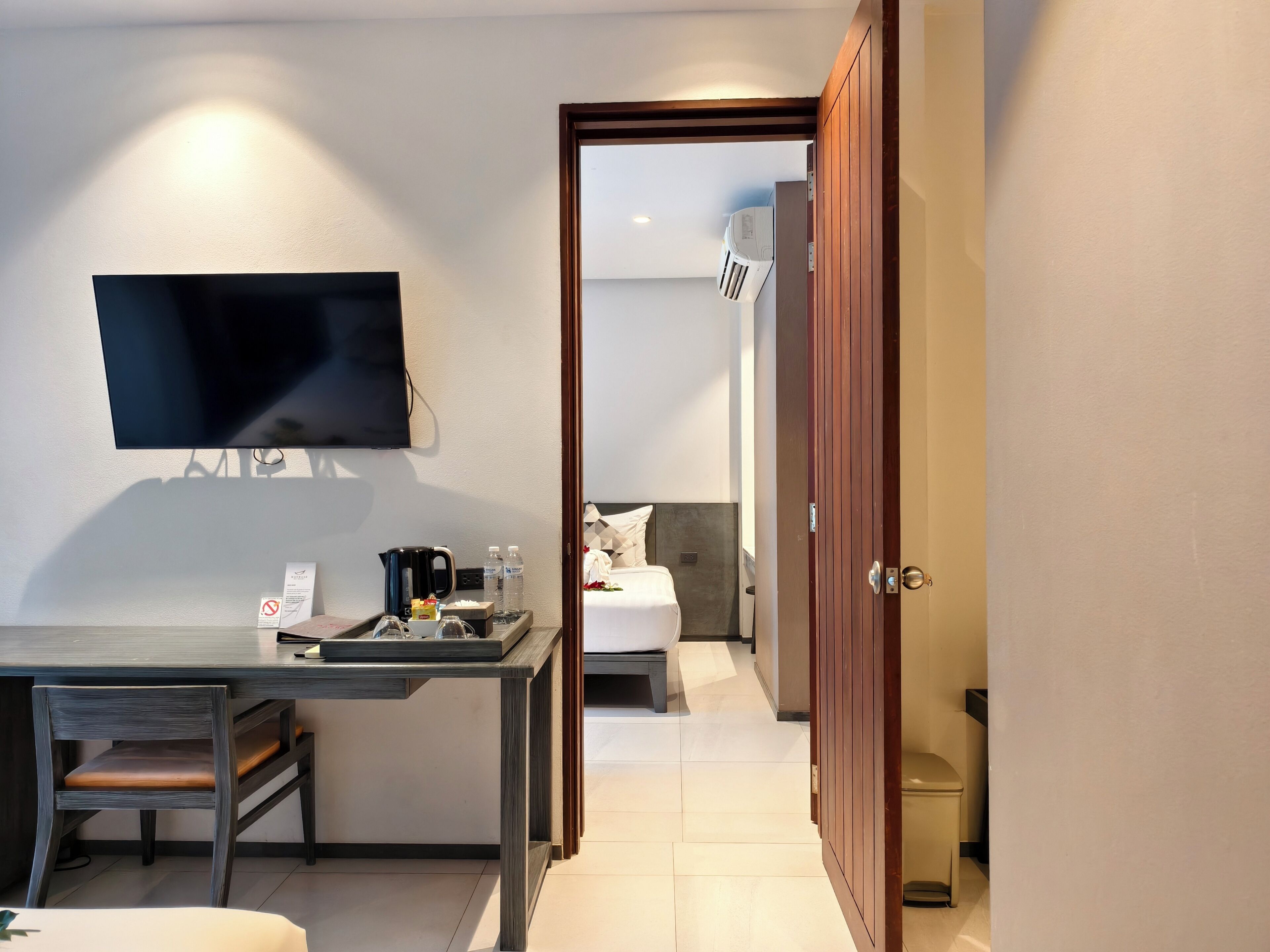 Quarto de hotel com televisão de tela plana na parede, escrivaninha com cafeteira, garrafas de água e bandeja.
