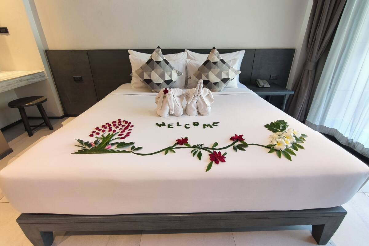 Un lit bien fait, agrémenté d’une pancarte « BIENVENUE », d’une petite statue et de quelques fleurs décoratives.