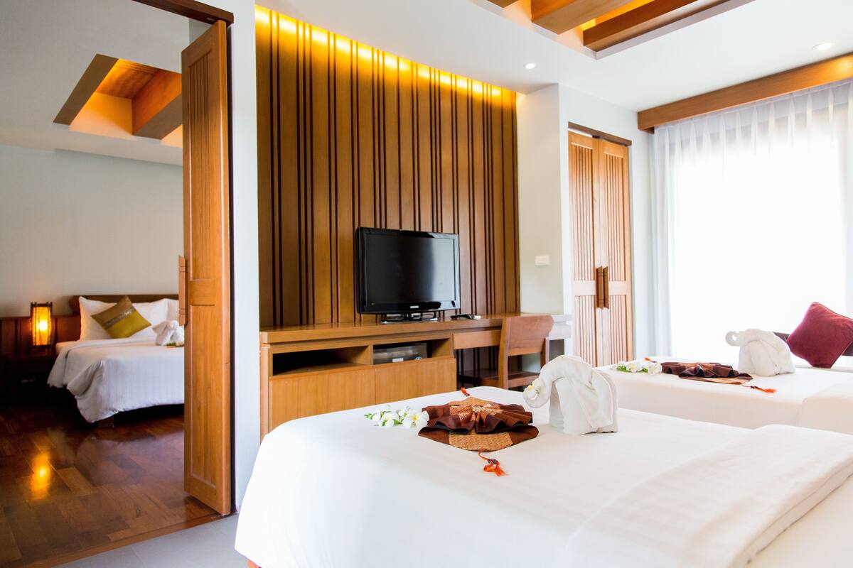 Une chambre d’hôtel avec deux lits, une télévision, des panneaux de bois et une fenêtre avec des rideaux.