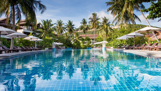 A swimming pool with clear blue water, surrounded by lounge chairs and umbrellas, with palm trees and a building in the background. - Maehaad Bay Resort (Ko Pha-ngan)