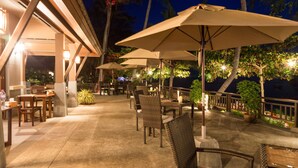 An outdoor patio area with tables and chairs, umbrellas, and a view of the ocean at night. - Maehaad Bay Resort (Ko Pha-ngan)