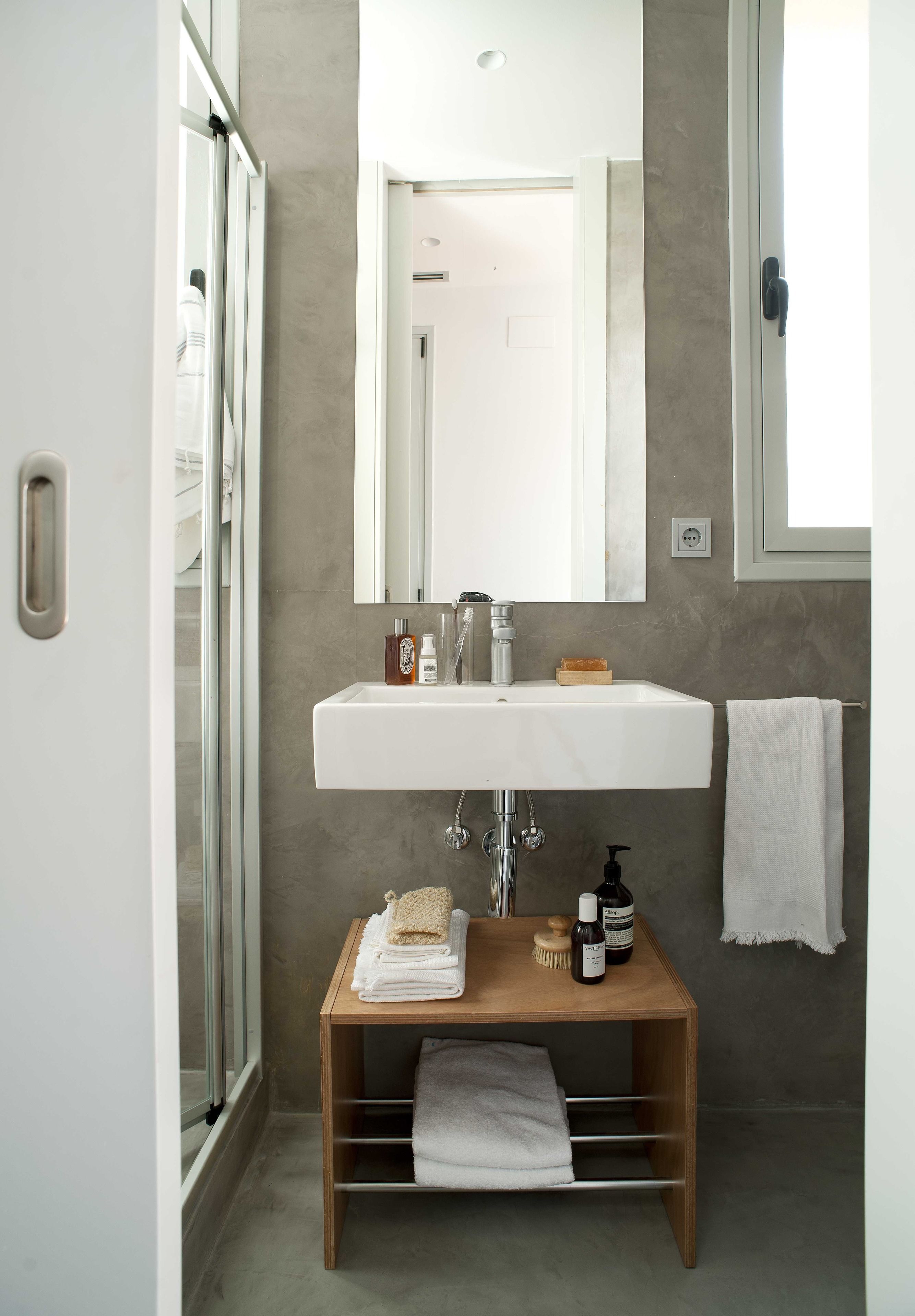 Une salle de bain moderne avec une porte de douche en verre, un lavabo blanc, un meuble-lavabo en bois et un porte-serviettes.