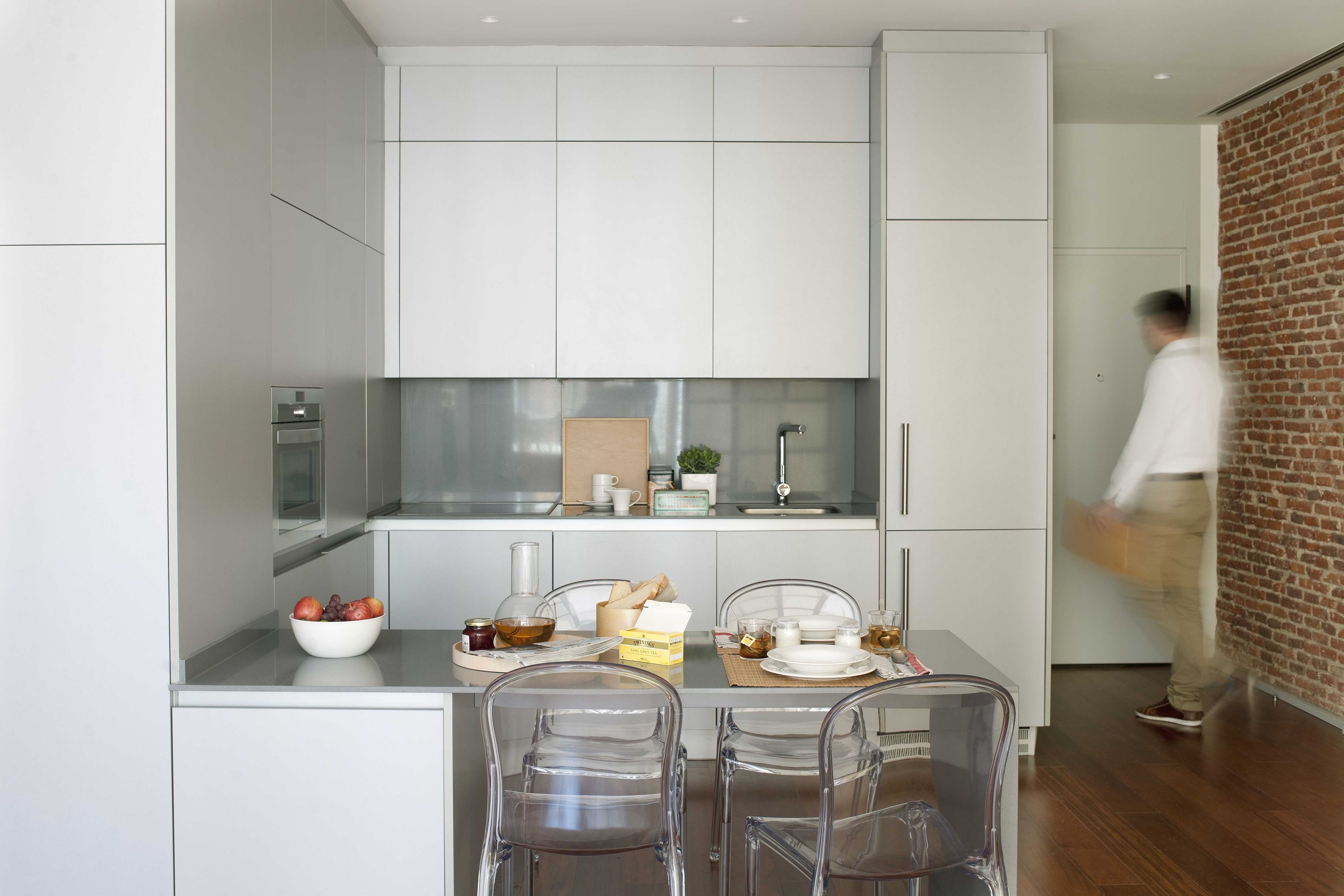 A modern kitchen with white cabinets, a stainless steel countertop, and a dining area with clear chairs.