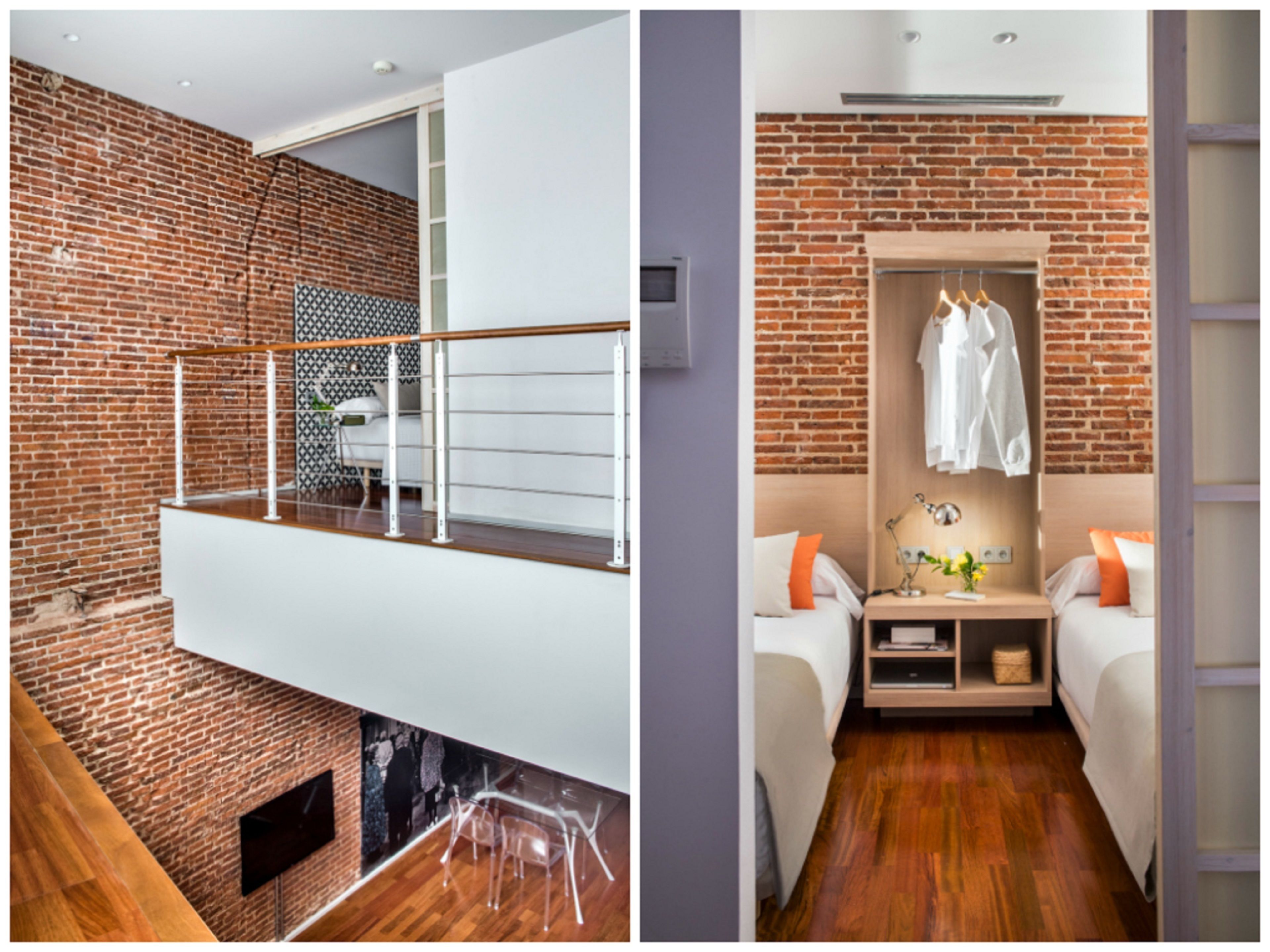 A modern room with a brick wall, a balcony with a glass railing, a bed with a nightstand, and a hanging clothes rack.