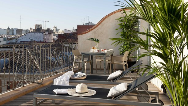Eine Dachterrasse mit Liegestühlen, einem Tisch mit einer Pflanze und Blick auf die Stadtlandschaft.