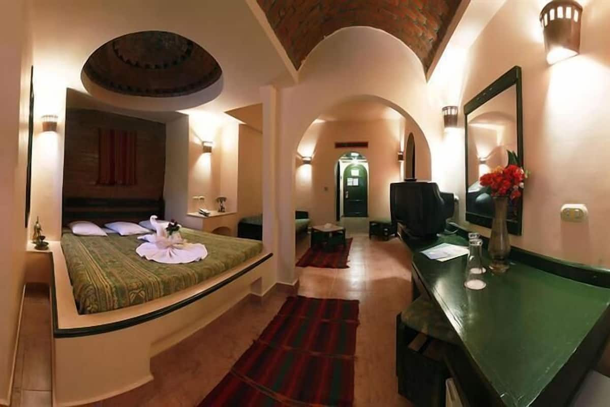 Hotelkamer met een gebogen bed, een bureau, een spiegel en uitzicht op de gang.