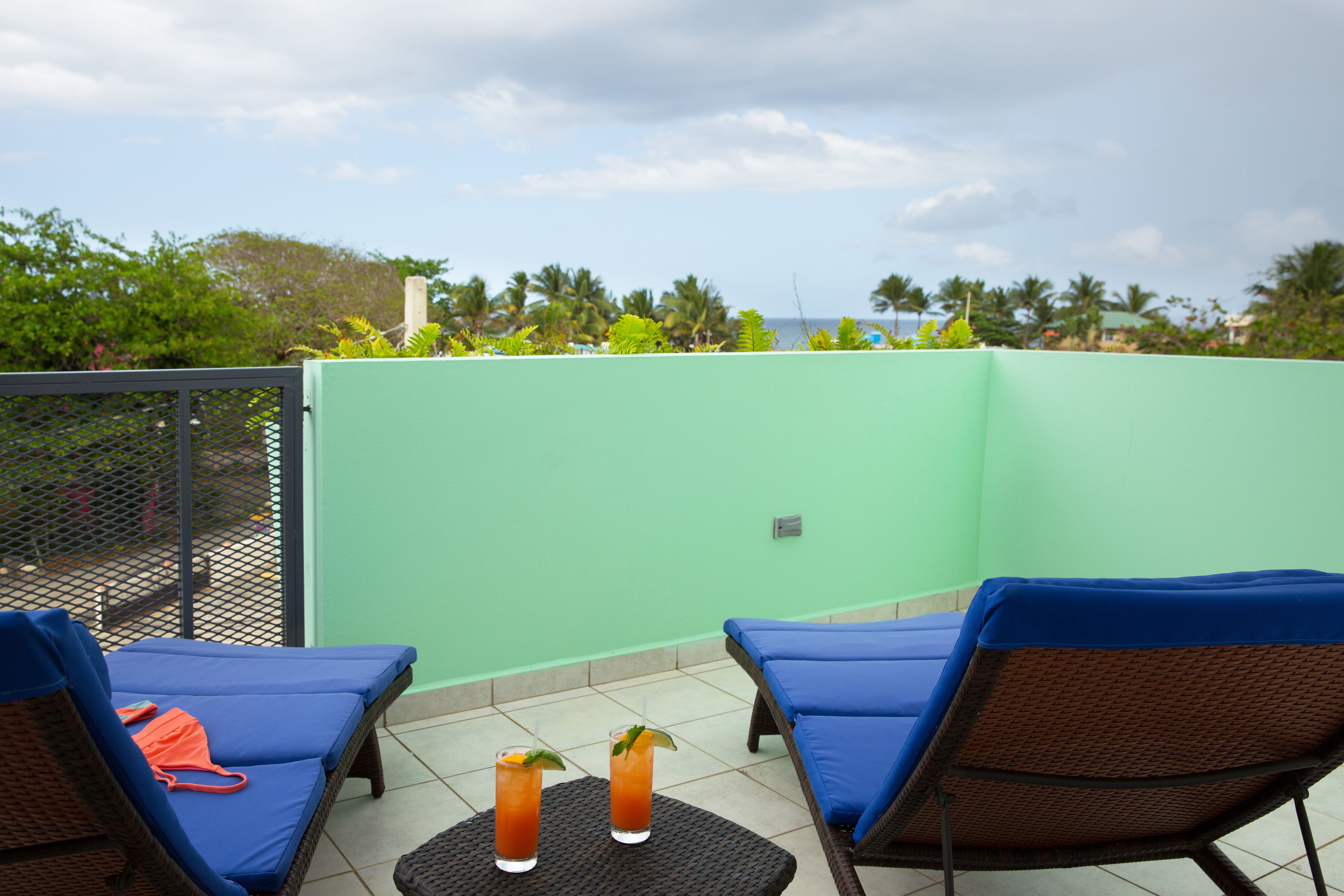 Una terraza en la azotea con dos sillones de descanso, una mesa con dos bebidas y vistas a palmeras y al océano.