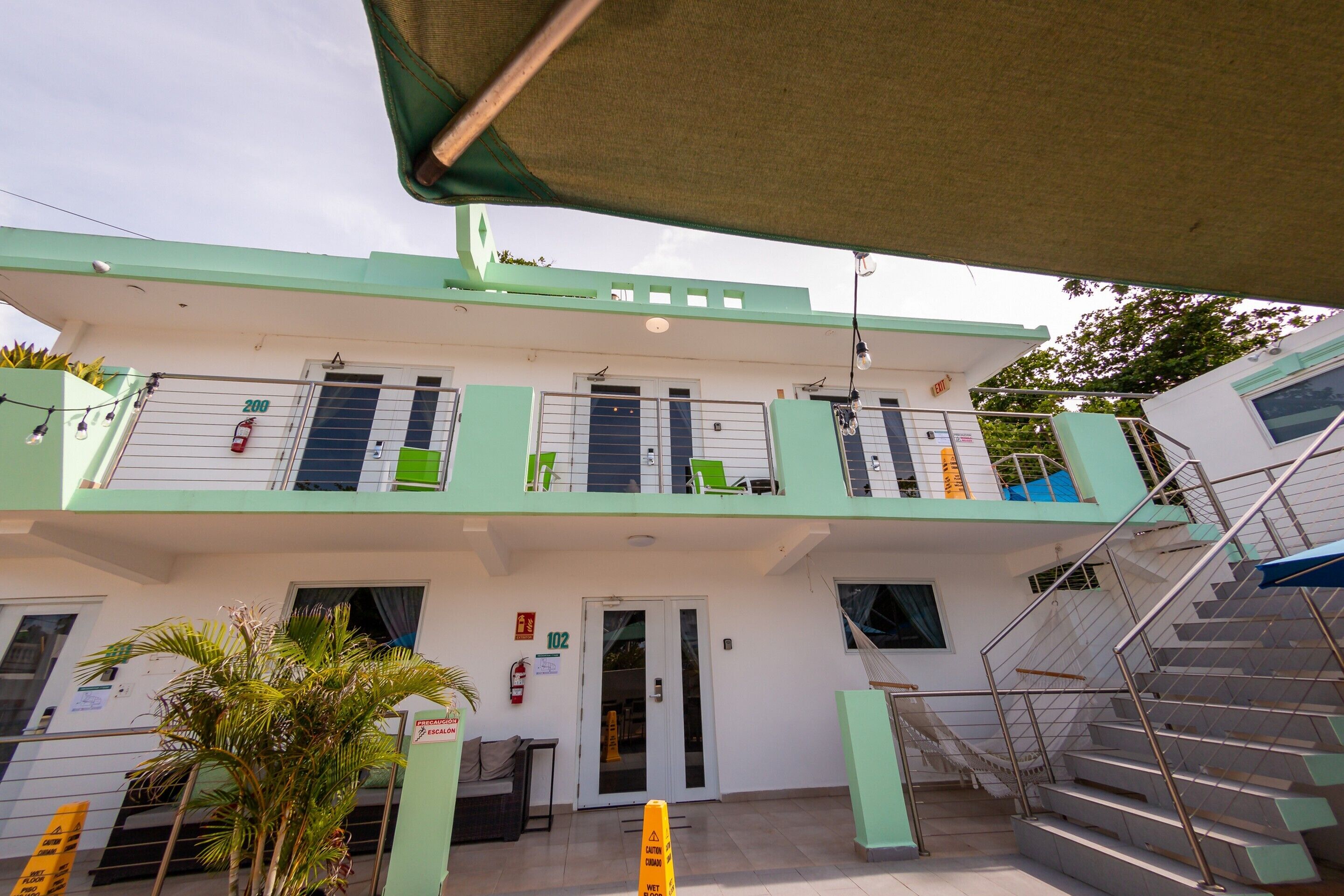 A two-story building with a green and white facade, a staircase on the right, and a door labeled '102' at the ground level.