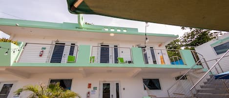 A two-story building with a green and white facade, a staircase on the right, and a door labeled '102' at the ground level.