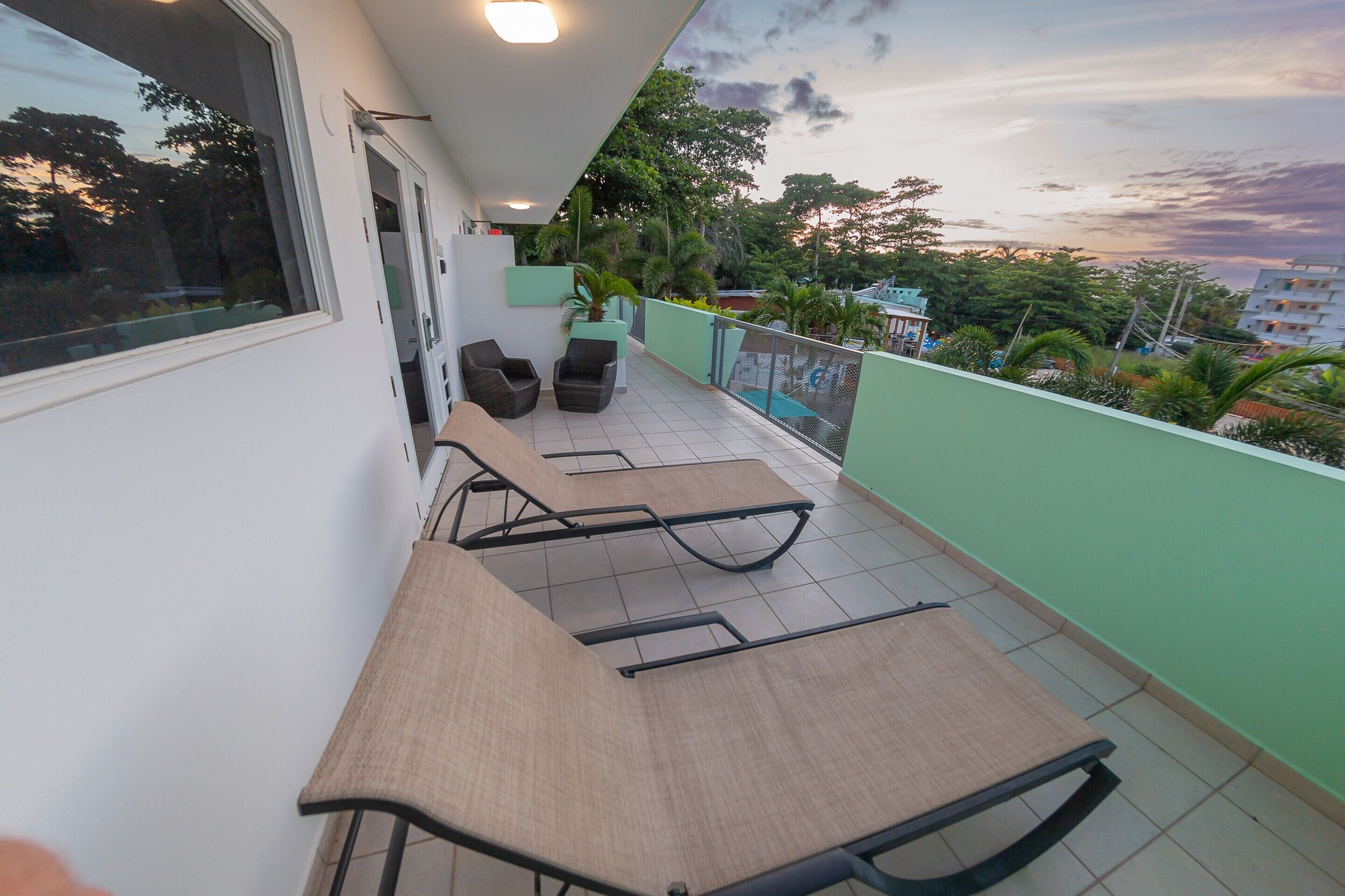 A balcony with a table and chairs, a view of the cityscape, and a sunset.