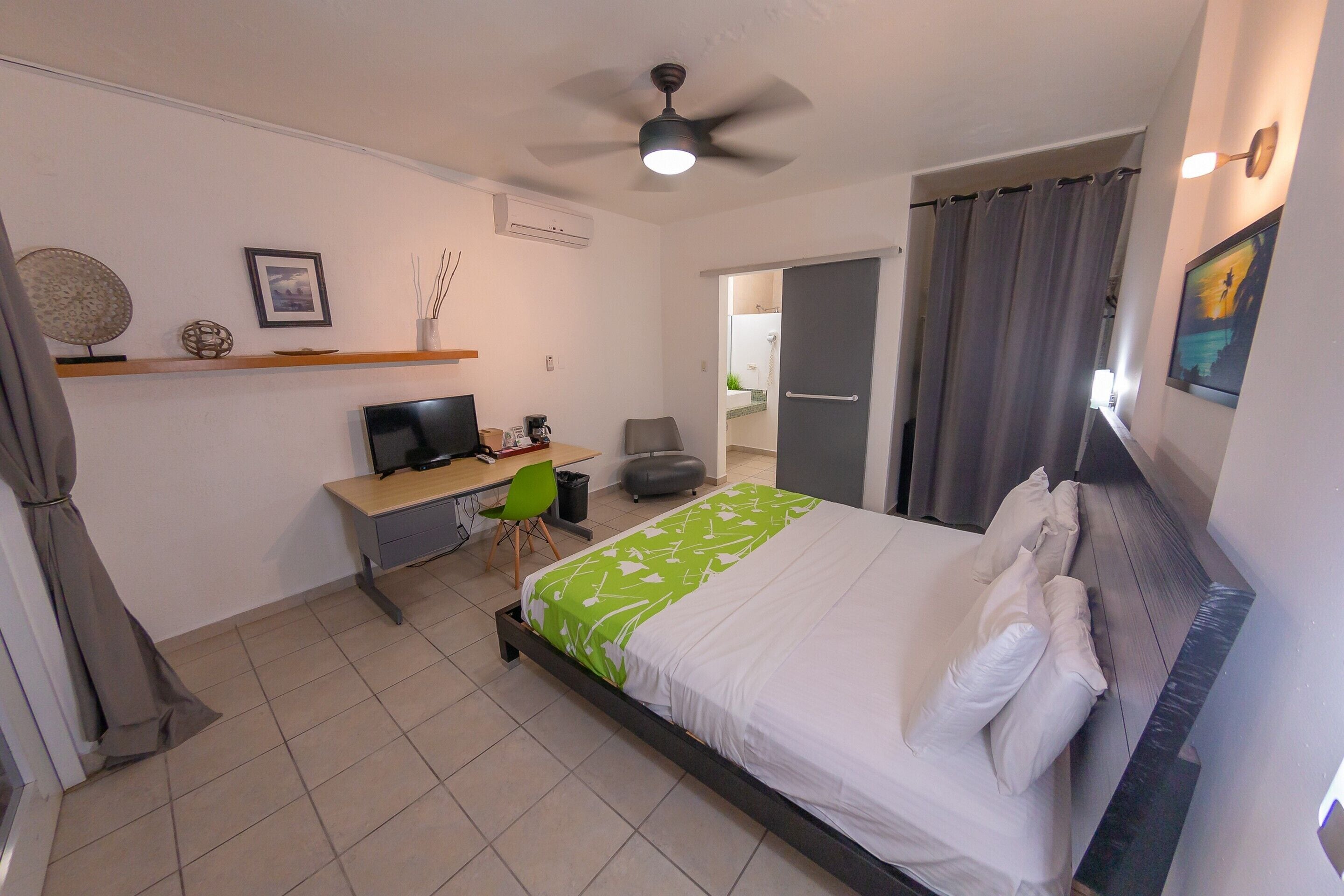 A hotel room with a bed, desk, chair, and a ceiling fan.