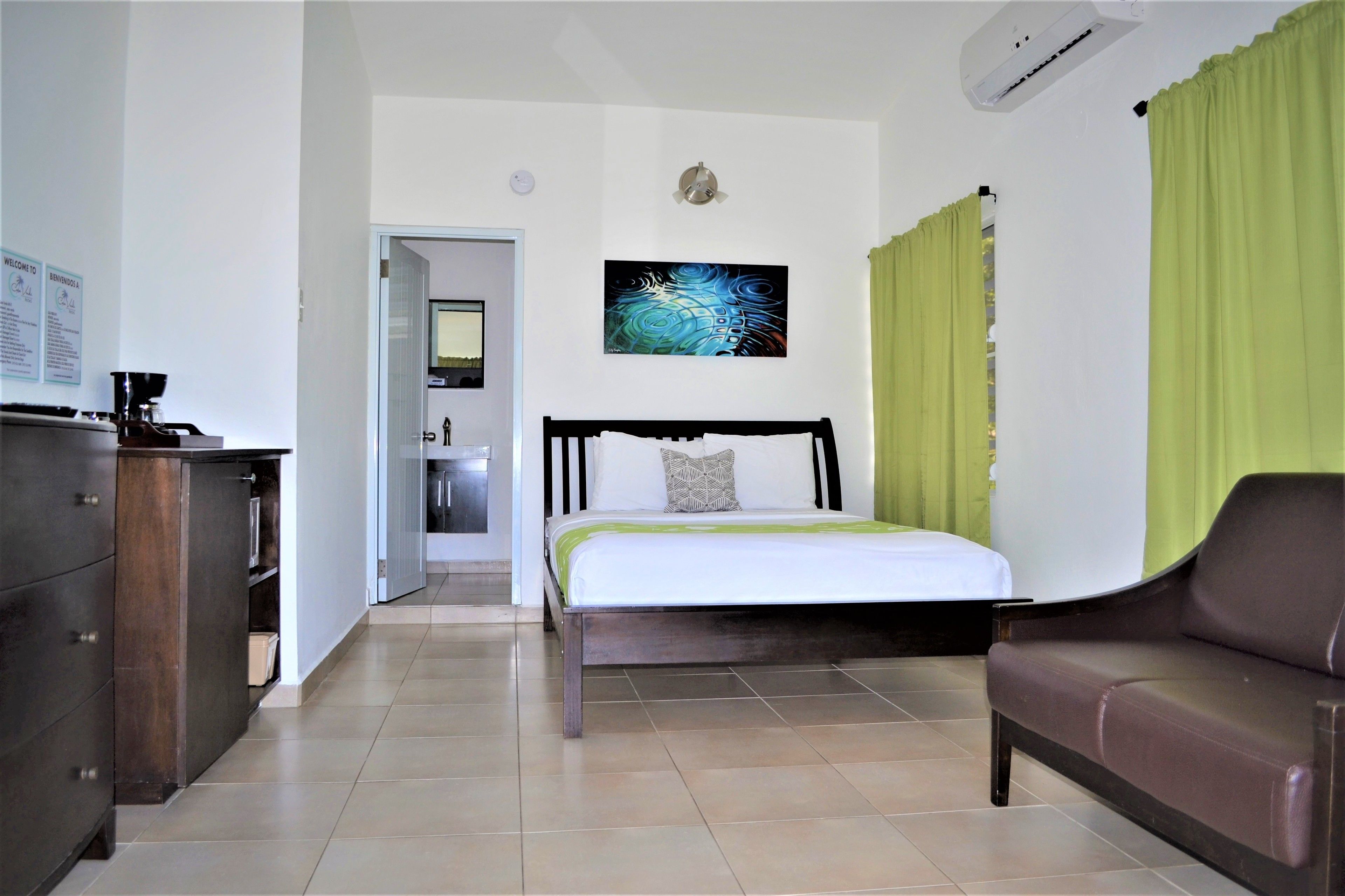 A hotel room with a bed, a brown leather sofa, a wooden dresser, and a painting on the wall.