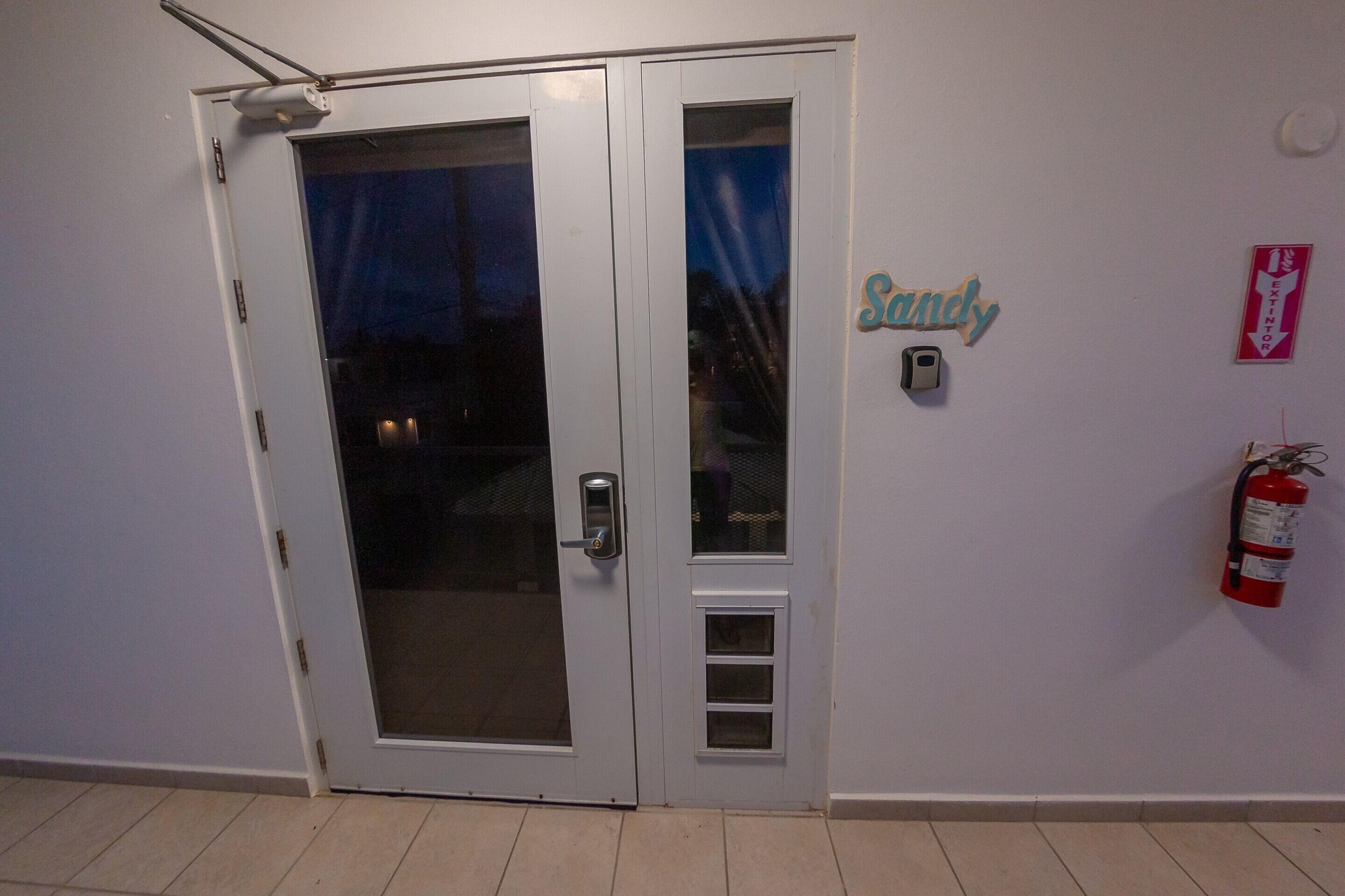 Ovi, jossa on lasiruutu, seinällä palosammutin ja kyltti, jossa lukee ”Sandy”.