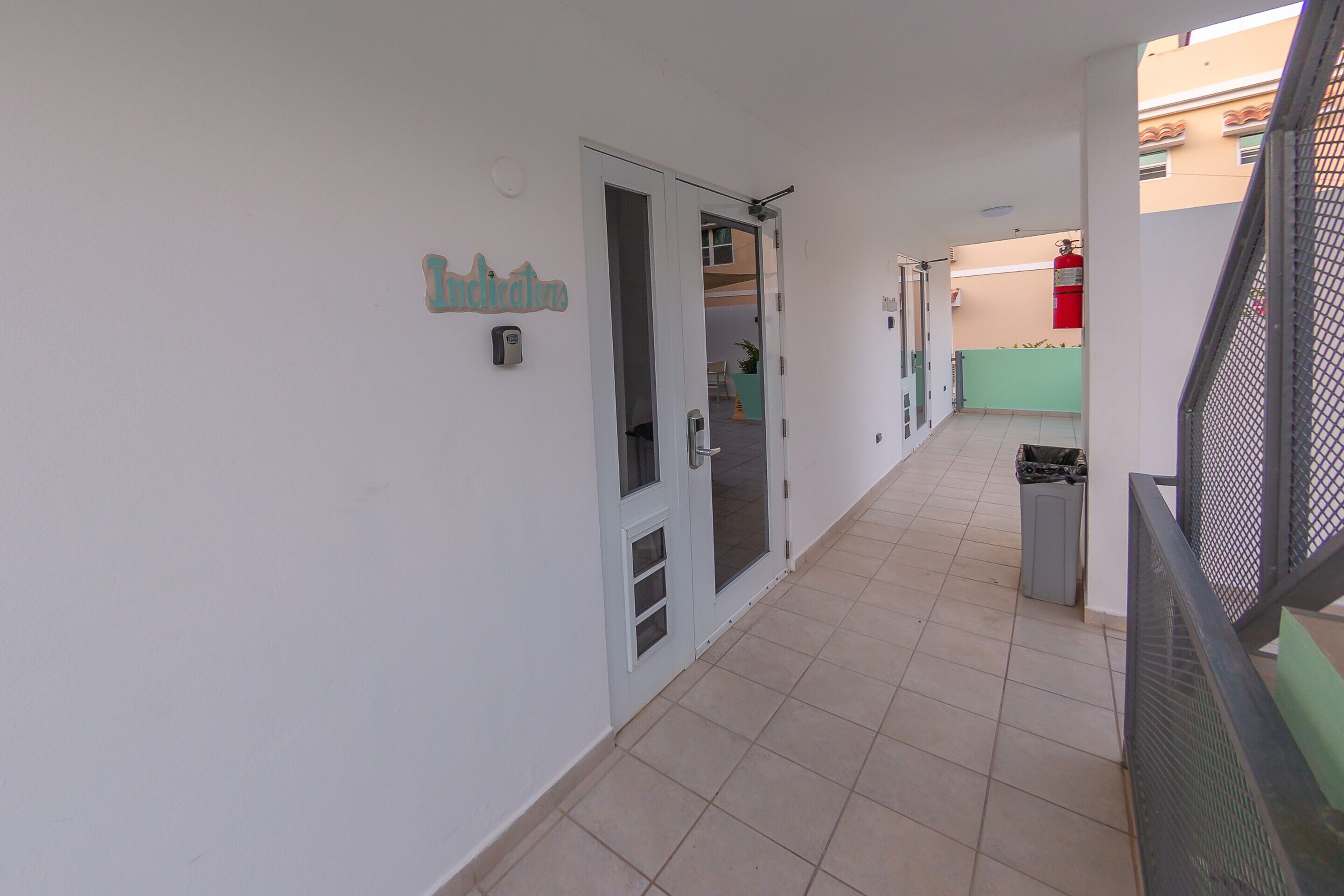 A corridor with a door labeled "Indications," a trash bin, and a fire extinguisher in the background.
