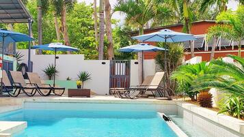 A swimming pool with lounge chairs and umbrellas, surrounded by tropical plants and trees.