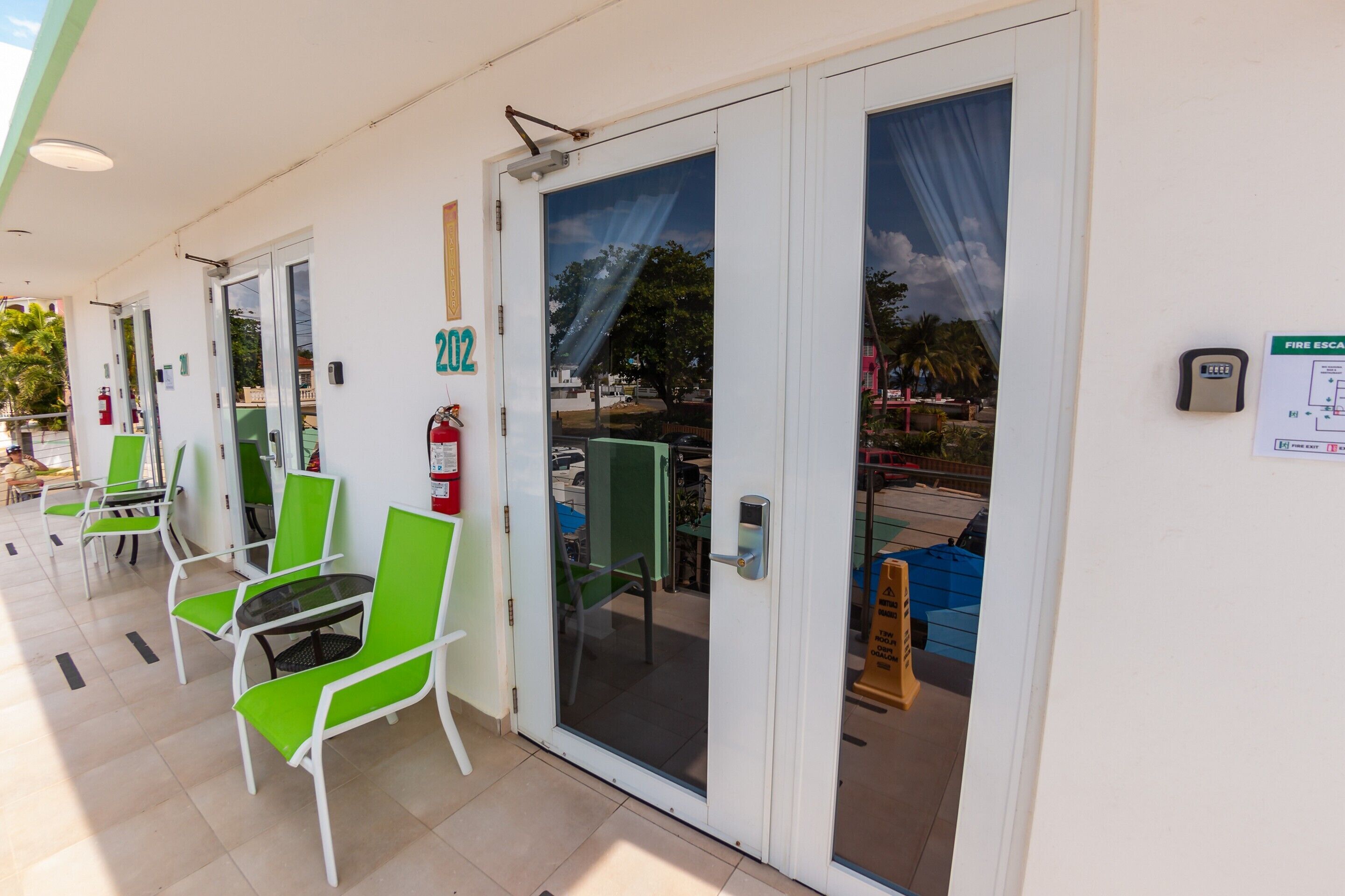A hotel entrance with numbered doors, green chairs, and a fire extinguisher.