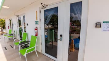 A hotel entrance with numbered doors, green chairs, and a fire extinguisher.