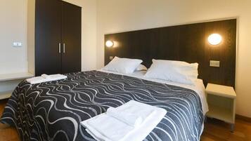 A hotel room with a large bed, a dark wardrobe, bedside tables, and a headboard with wall-mounted lights.