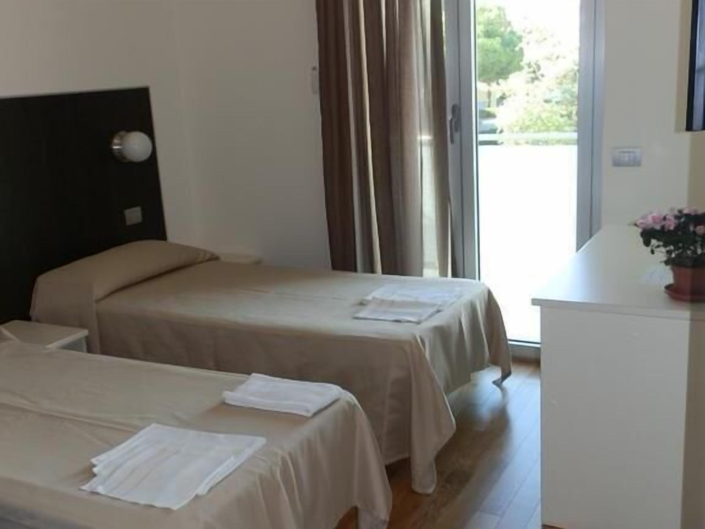 A hotel room with two beds, a small desk, and a window with curtains.