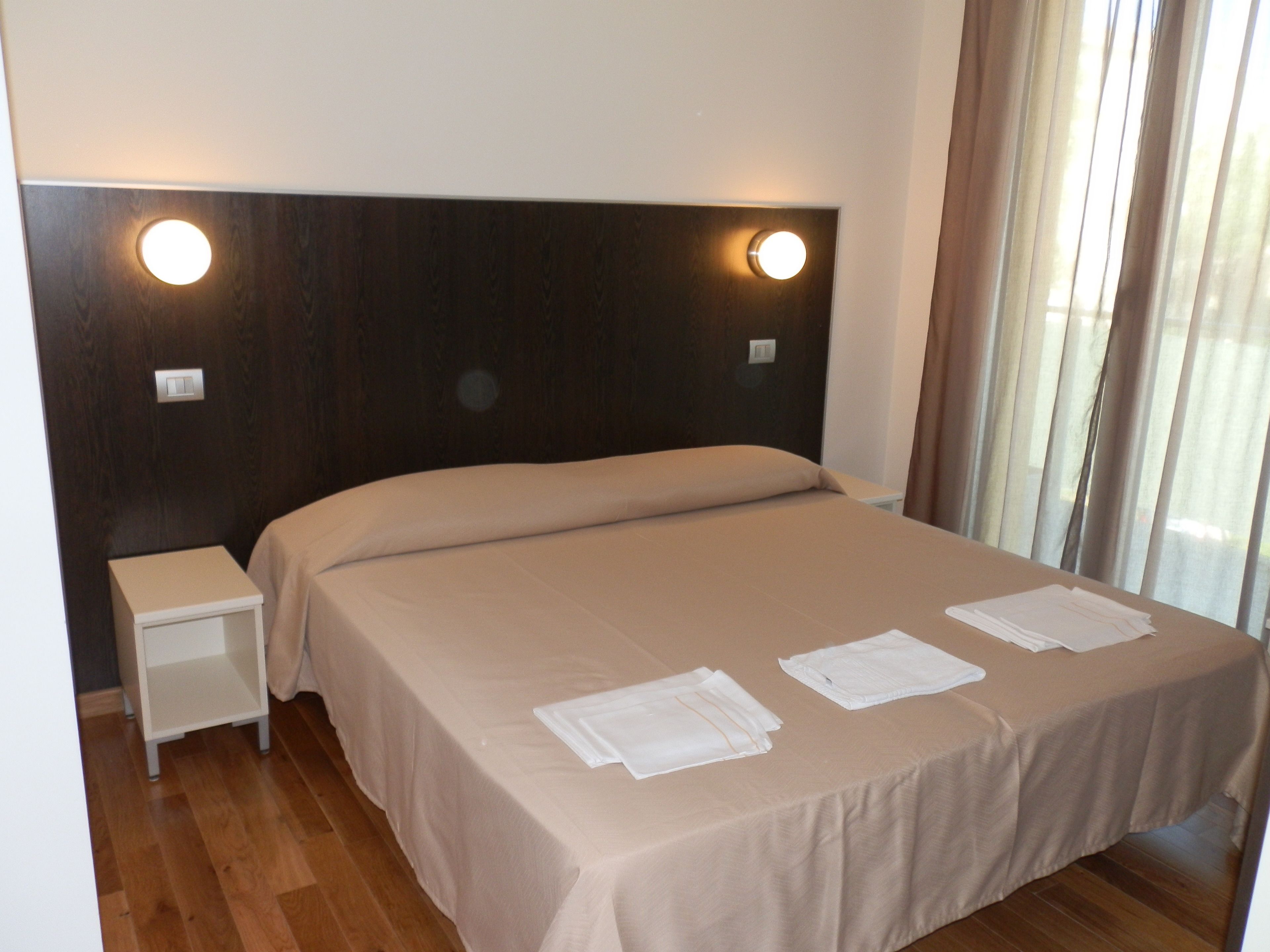 A neatly made bed with a headboard, a bedside table, and two wall-mounted lights.