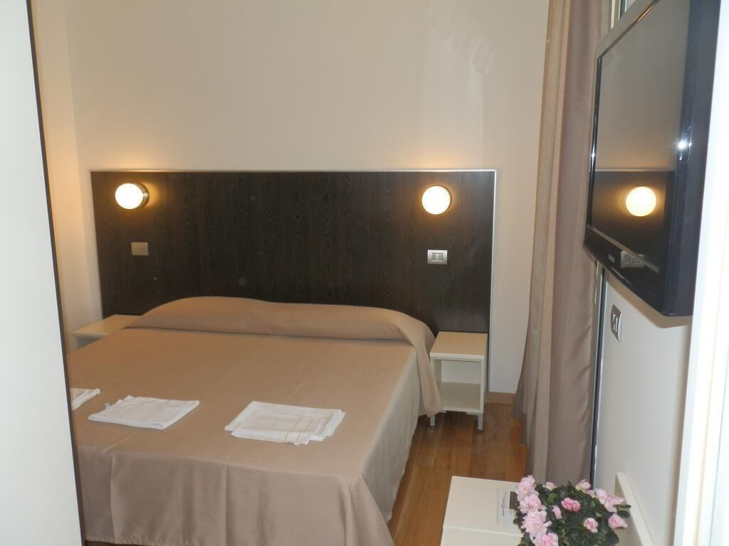 Une chambre d’hôtel avec deux lits, un téléviseur à écran plat et une petite table sur laquelle est posé un vase de fleurs.