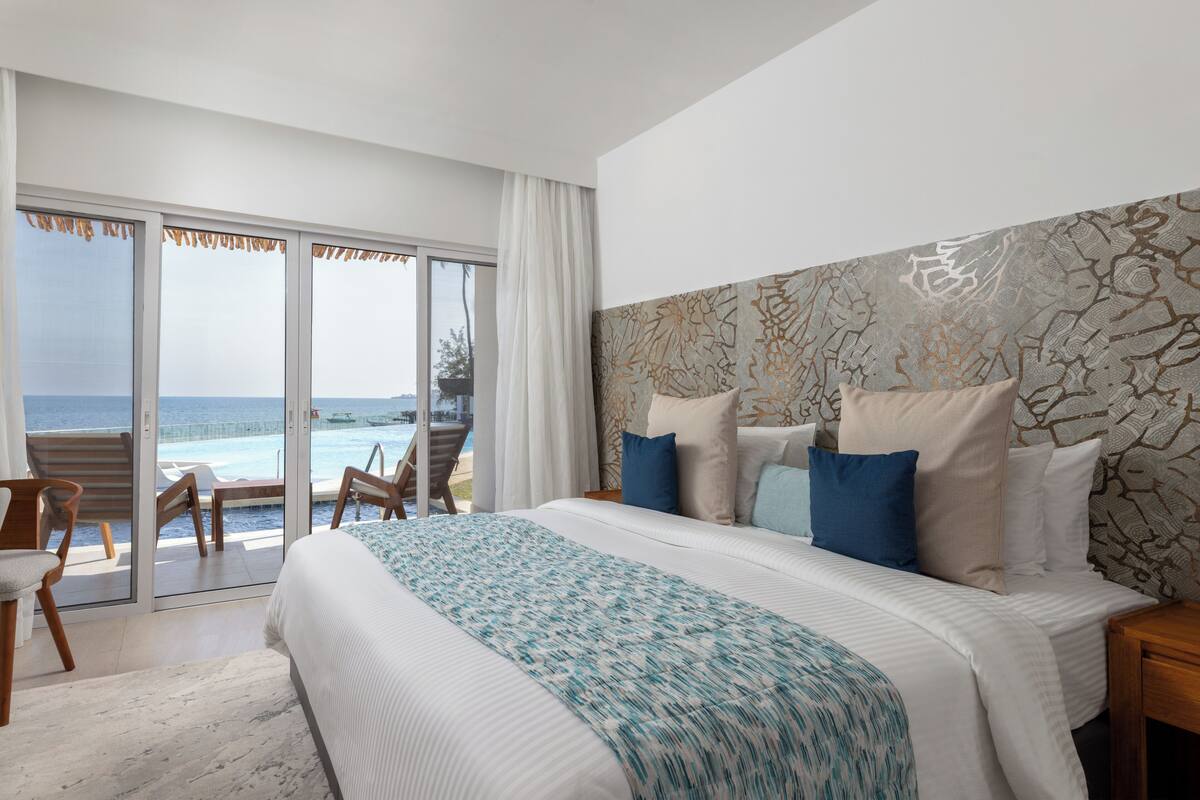 A bedroom with a large bed, a view of the sea, and a balcony with a pool.