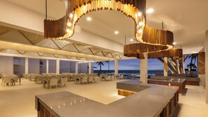 A spacious indoor area with a long counter, multiple tables, and chairs arranged for dining or socializing. - Bamburi Beach Hotel - All Inclusive (Mombasa)