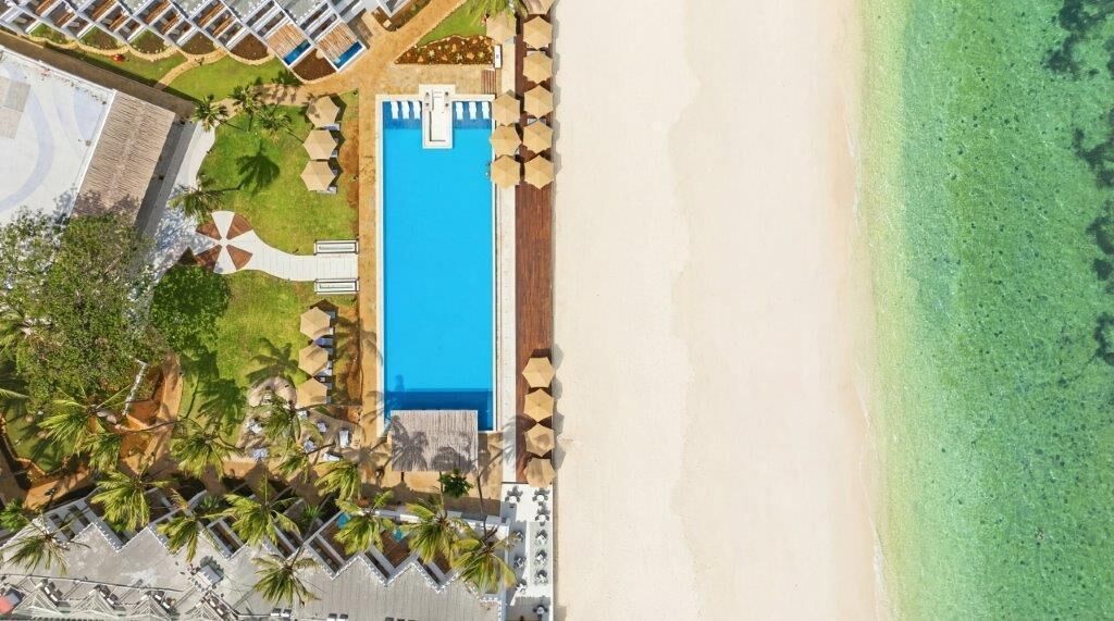 Luftaufnahme eines Resorts mit Schwimmbad, Strand und Palmen.