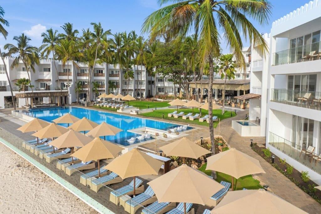 A resort with a swimming pool, sun loungers, and palm trees.