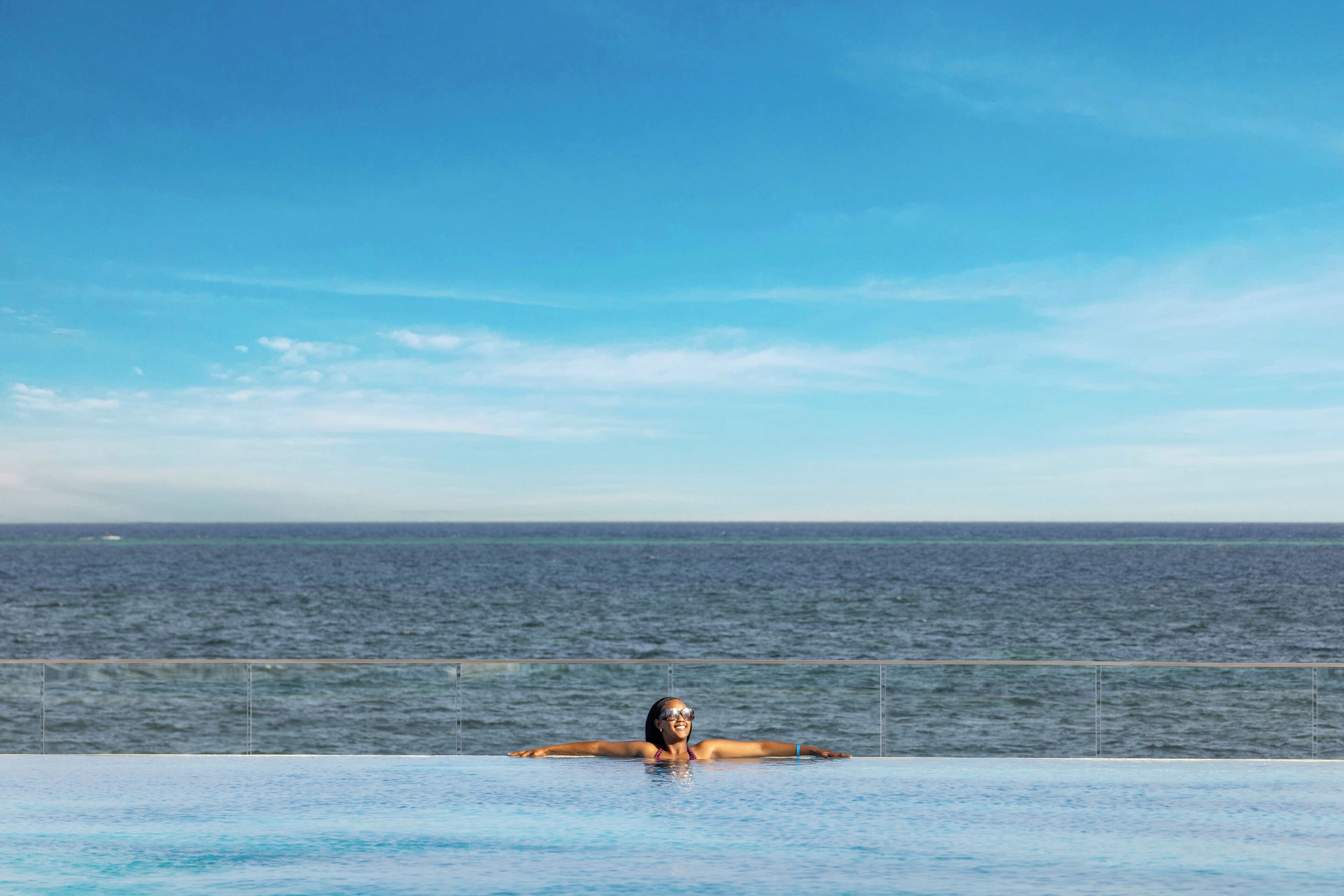 Eine Person entspannt sich in einem Infinity-Pool mit Blick auf den Ozean.