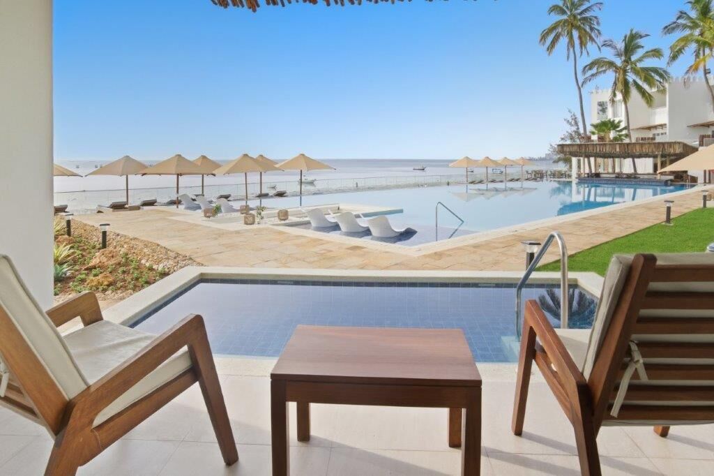 Zona de piscina con sillas de descanso y sombrillas, con vista a una playa.