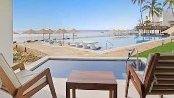 Zona de piscina con sillas de descanso y sombrillas, con vista a una playa.