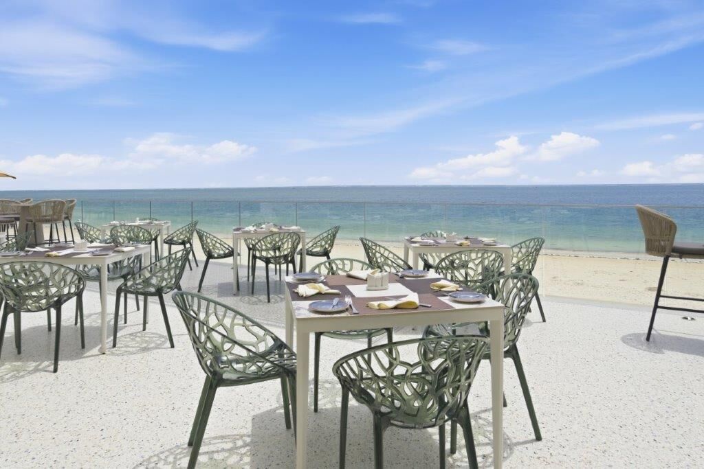 Outdoor dining tables with chairs on a beach, overlooking the ocean.