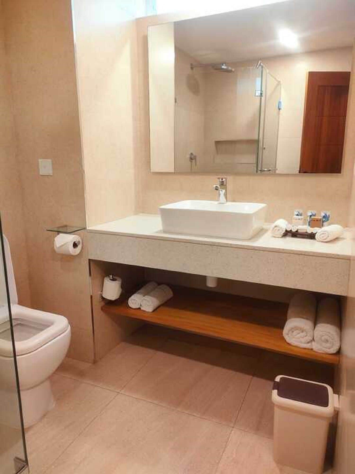 Une salle de bain avec un lavabo blanc, un miroir, des toilettes et une étagère avec des serviettes.