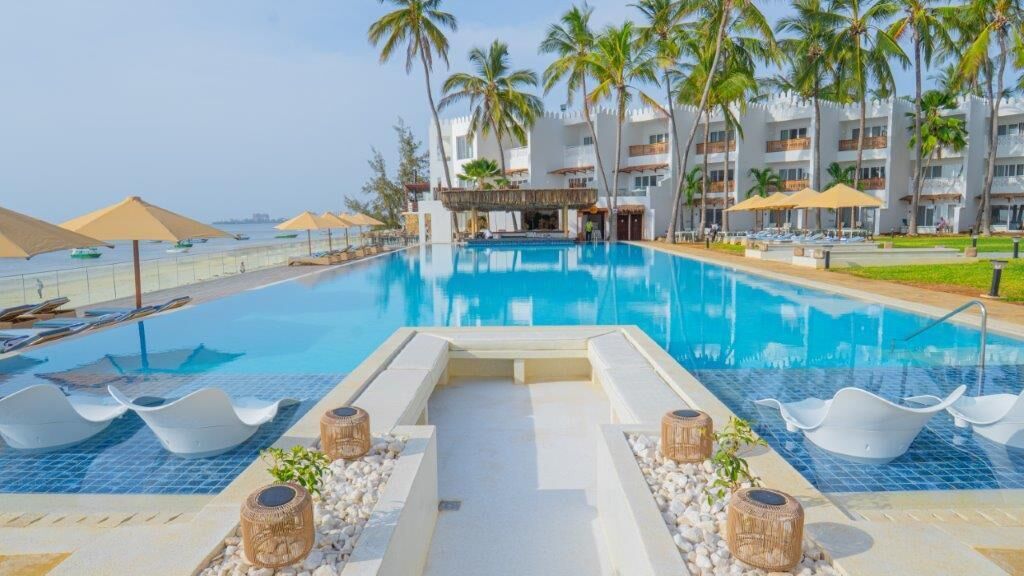 A swimming pool with lounge chairs, palm trees, and a building with balconies.