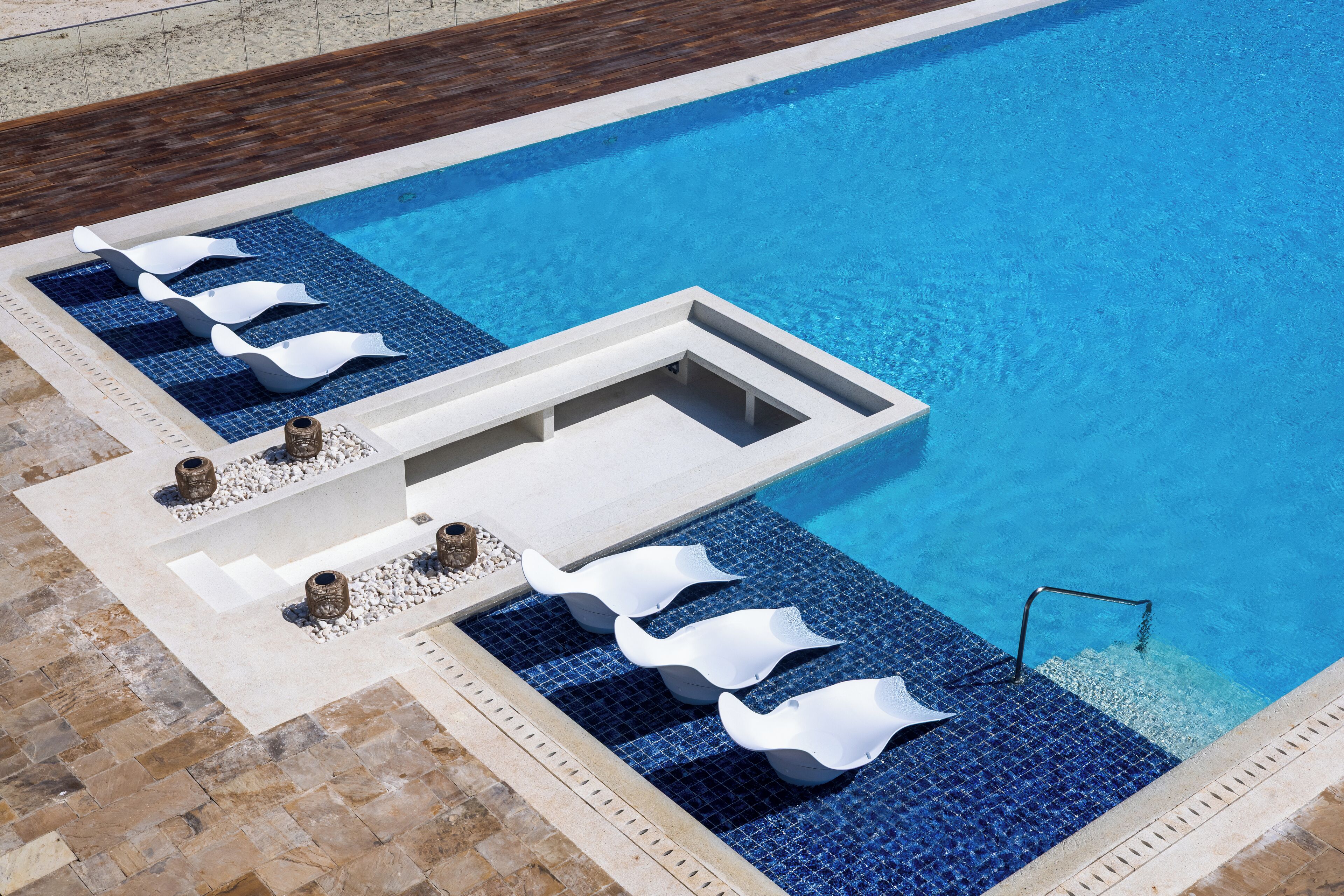 A swimming pool with a tiled deck, a built-in seating area, and a small water feature.