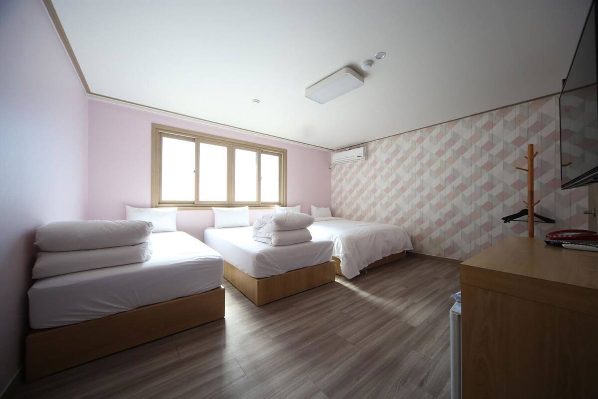 Ein Zimmer mit zwei Betten, Holzboden, einem Fenster und einem Kleiderständer.