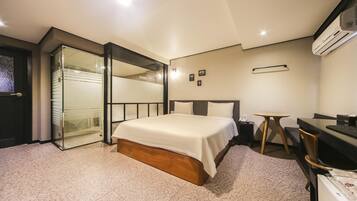 A modern hotel room with a large bed, a desk, and a chair. There is a sliding glass door leading to a balcony.