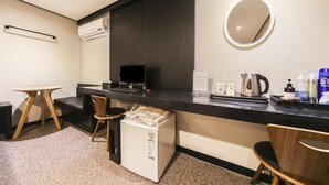 Habitación de hotel compacta con kitchenette, una mesita, dos sillas, refrigerador, cafetera y espejo en la pared.