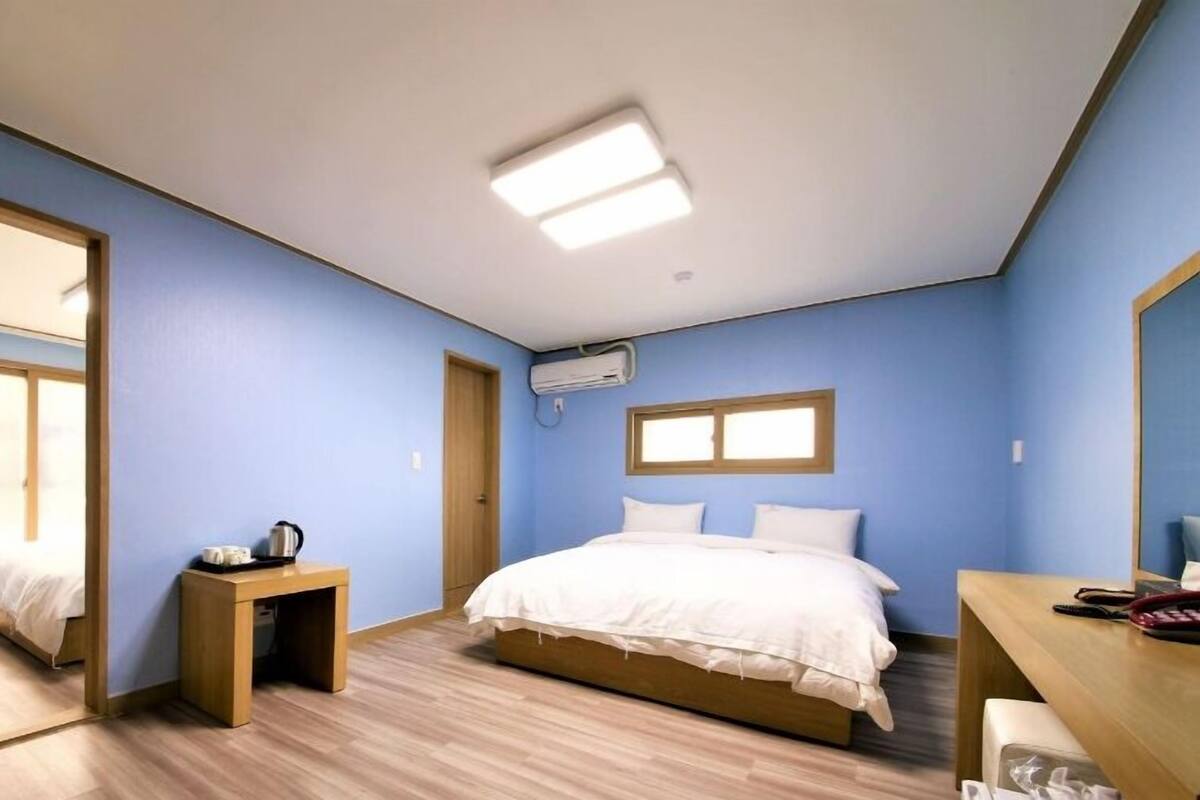 Ein Schlafzimmer mit einem Bett, einem Nachttisch aus Holz, einem Schreibtisch und einem Spiegel.