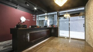 Un área de recepción con un mostrador oscuro, un candelabro y un amplio ventanal con vista a la calle.