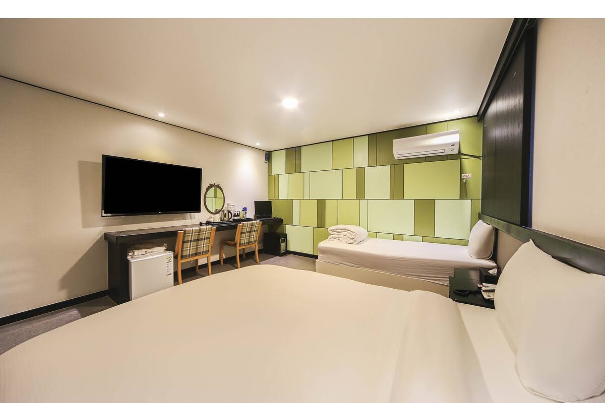 Ein Hotelzimmer mit einem Bett, einem Schreibtisch mit Stuhl, einem Fernseher und einer Wandklimaanlage.