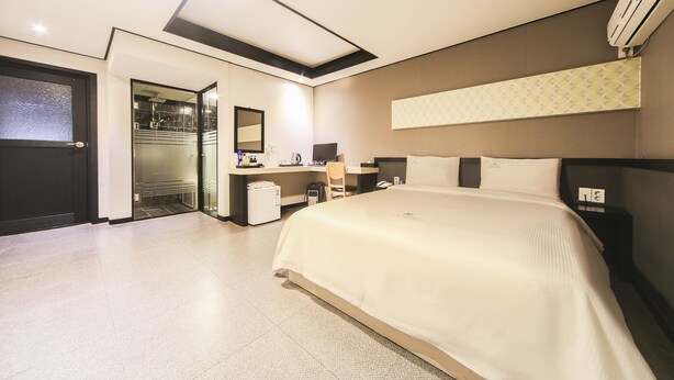 Una habitación de hotel moderna con una cama grande, un escritorio con una silla, un espejo y un armario.