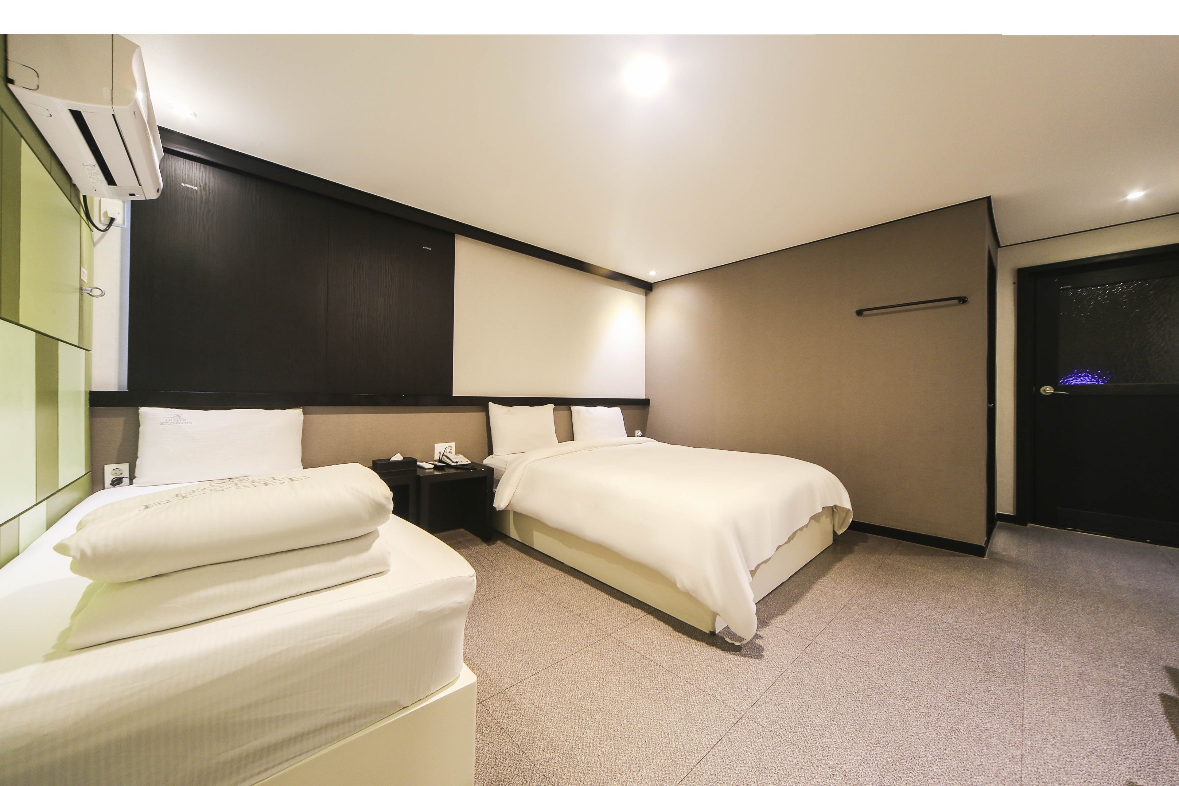 Habitación de hotel con dos camas, una mesita de noche, aire acondicionado de pared y una puerta con pomo.
