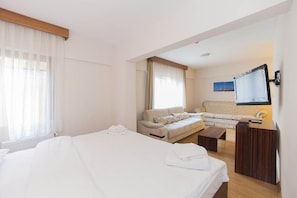 A hotel room with a large bed, a sofa, a small table, and a TV mounted on the wall.