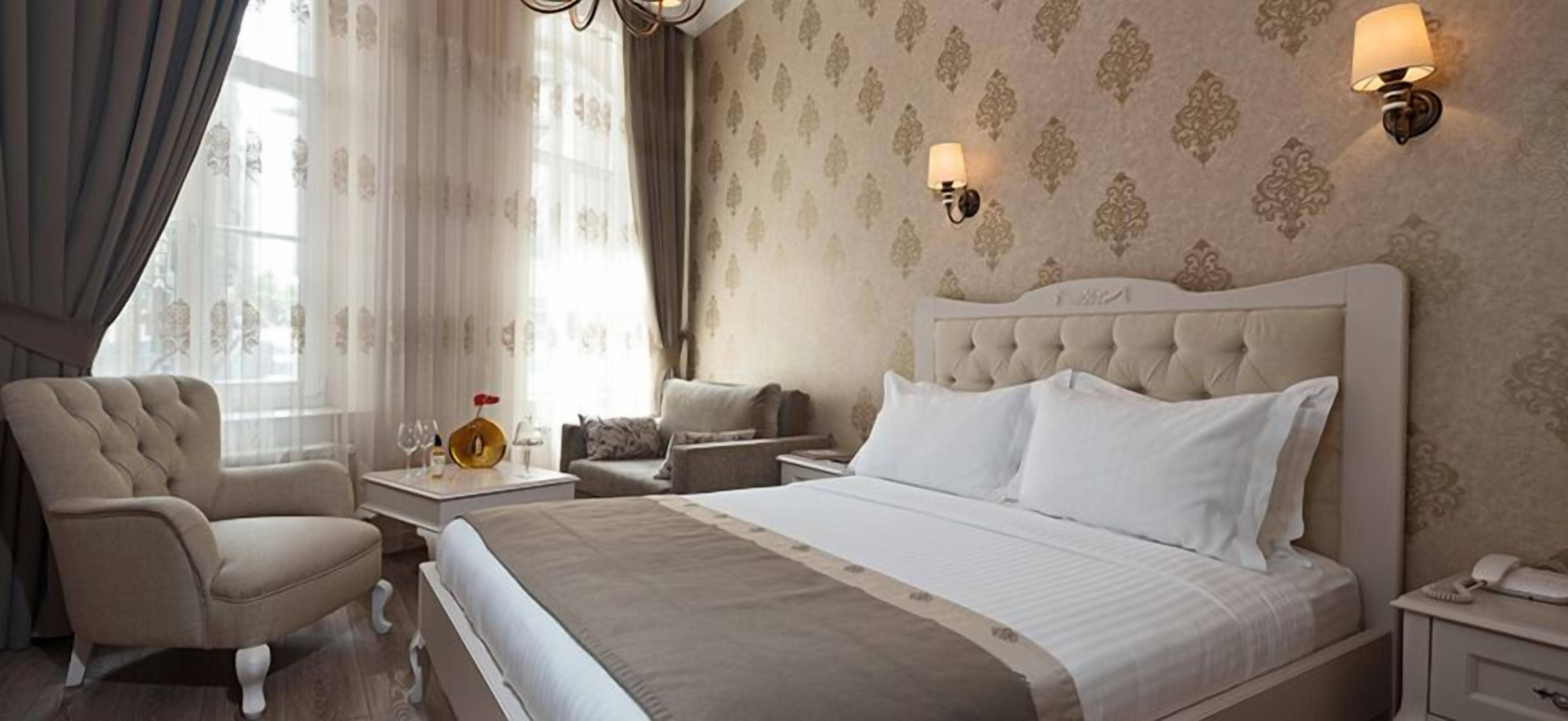 A hotel room with a large bed, a chair, a bedside table with a lamp, and a wall-mounted light fixture.