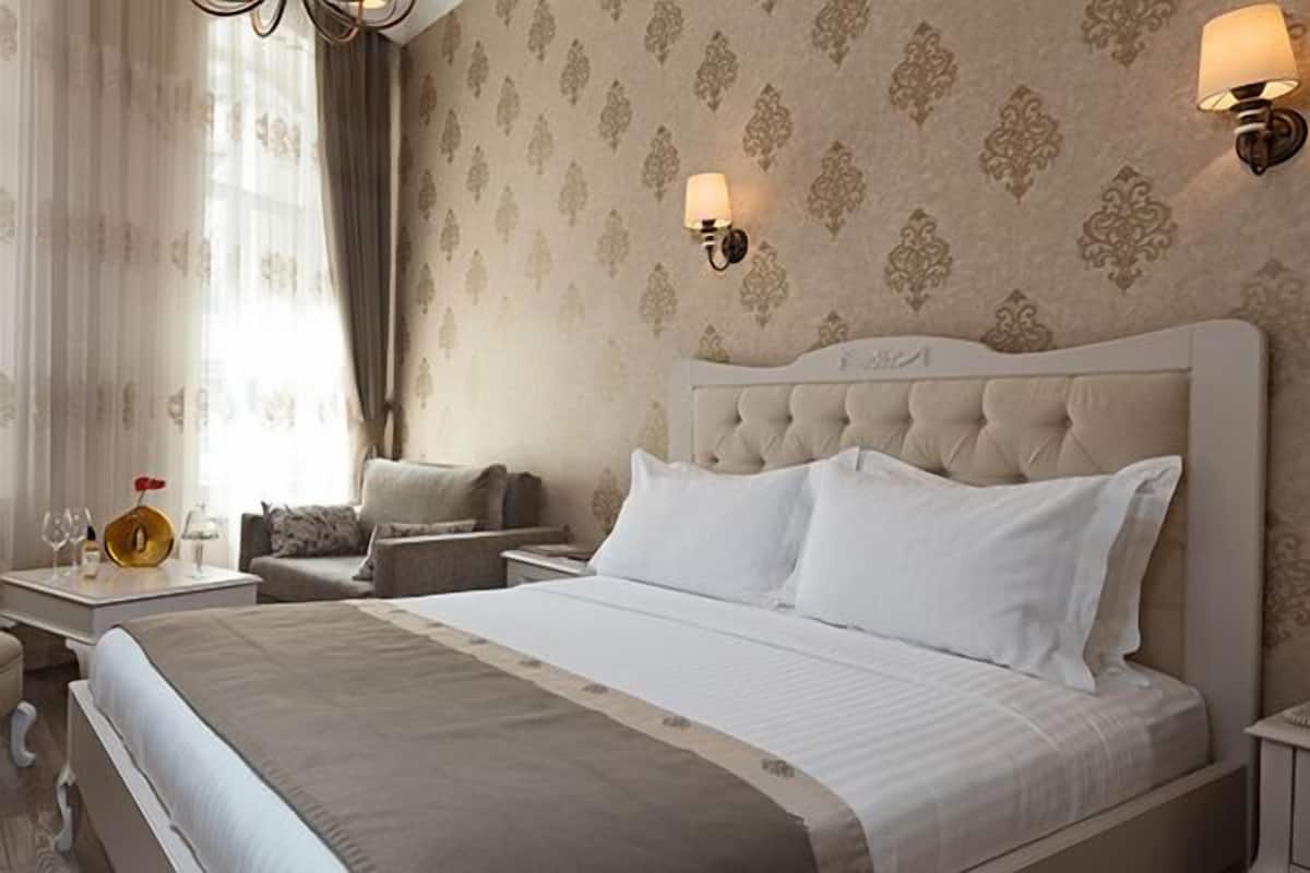 A hotel room with a large bed, a sitting area with a chair and a small table, and two wall-mounted lamps.