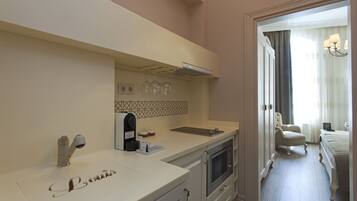 A modern kitchen with a built-in oven, a coffee machine, and a sink. There is a dining area with a chair and a table.