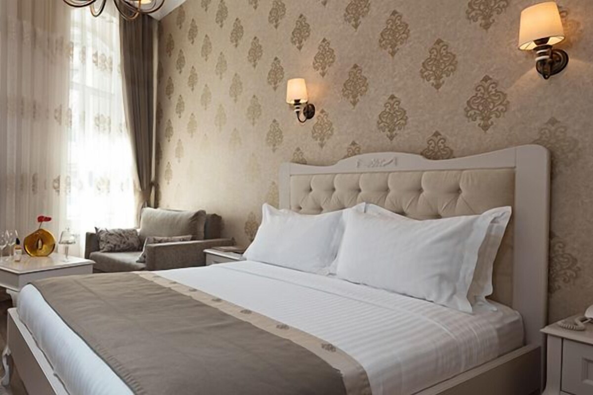 Ett hotellrum med en stor säng, en sittgrupp med en fåtölj och ett litet bord samt två väggmonterade lampor.